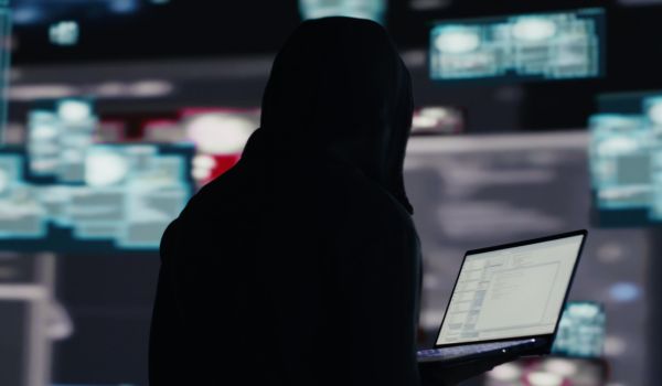 Person in black hood holding a laptop