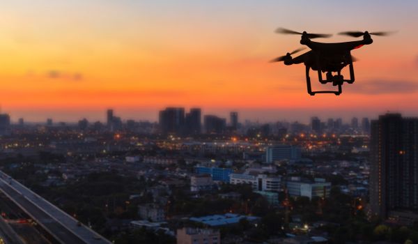 Silhouette of drone flying above city at sunset