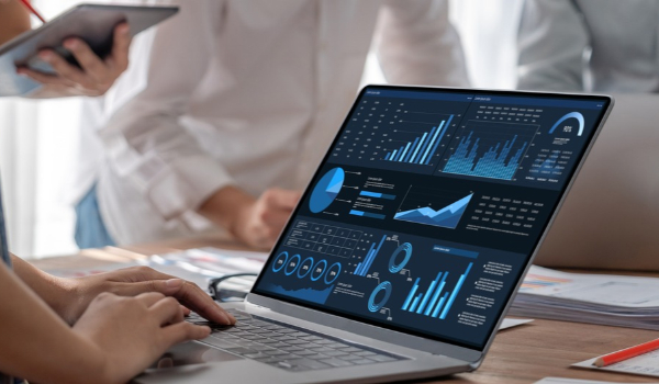 A person works on a laptop displaying data analytics dashboards and charts during a team meeting.