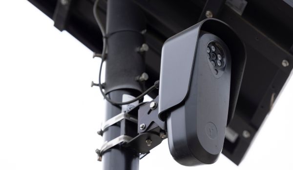 An AI Flock camera surveils a city street for car license plates on a dark cloudy day