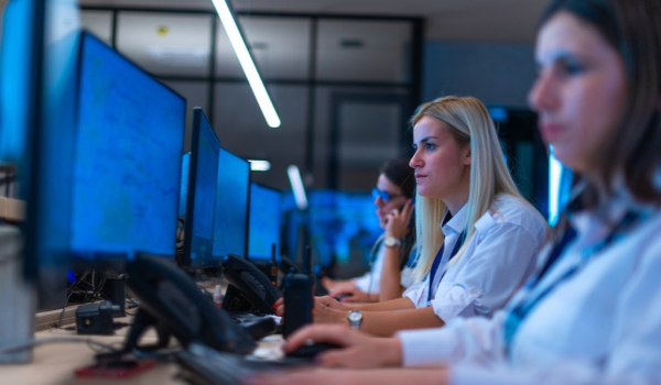 Security operations center staff working at computer monitors in a control room, with one employee speaking on a phone.