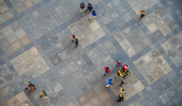 Aerial top-down view of pedestrians walking across a tiled public plaza or square.