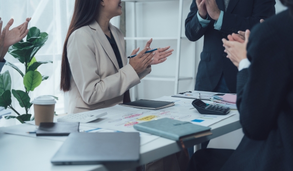 A business team clapping in celebration around a conference table during a successful meeting.