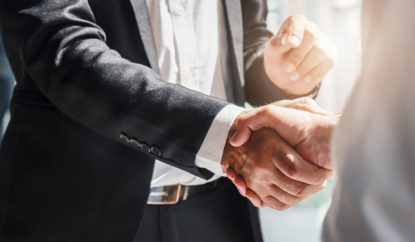 A close-up view of two business professionals shaking hands in a brightly lit setting.   