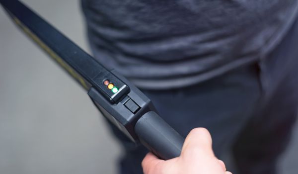 Guard with a metal detector checking a man for weapons and metal objects