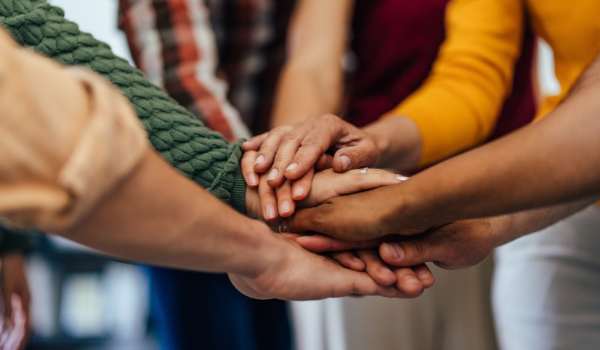 A diverse group of people stacking their hands together in the center for a team huddle.
