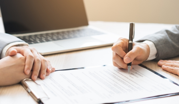Close up of business people hands signing contract agreement document on clipboard at desk in office