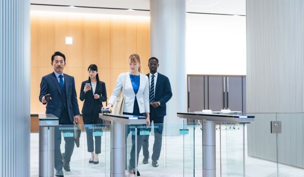 Business professionals tapping ID badges to pass through electronic security turnstiles in a corporate lobby.