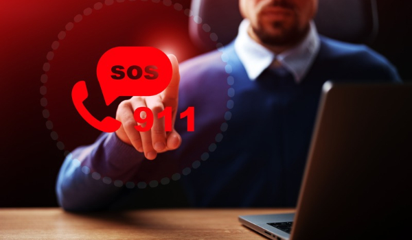 Person at a laptop reaching toward a digital emergency icon displaying SOS, 911 and a telephone symbol.