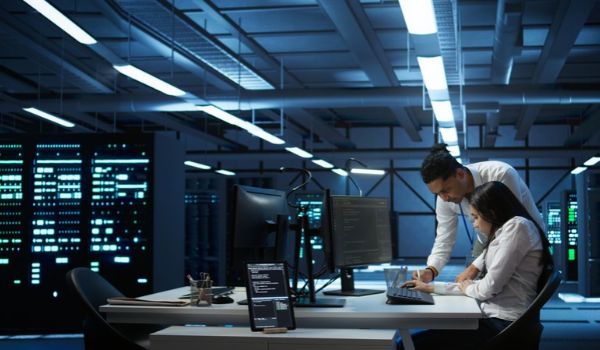 Two professionals review information at a workstation surrounded by server racks in a data center.
