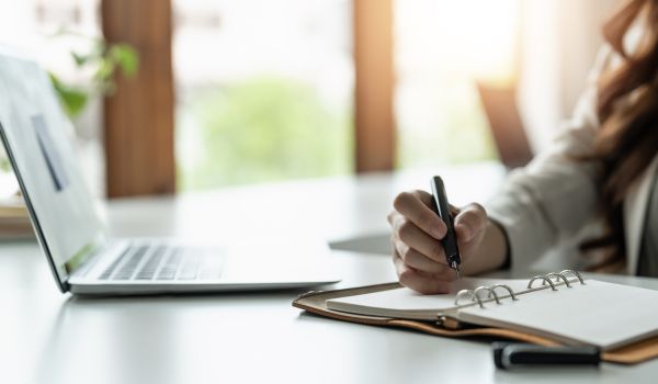 Woman participating in remote training, uses laptop and notebook.