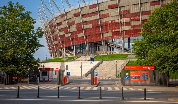 Exterior view of the National Stadium showcasing its red and silver mesh facade and entry gate under clear sky