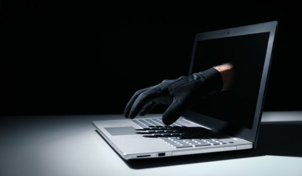 Black-gloved hand reaching out of a laptop screen toward the keyboard, illustrating cybercrime.