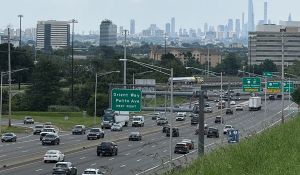 A busy highway in Rutherford, New Jersey, with traffic passing green exit signs and the New York City skyline visible in the distance.