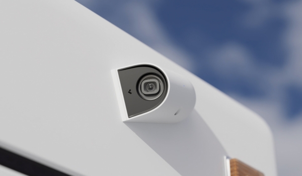 A close-up of a white, modern security camera mounted on the exterior wall of a building against a blue sky.