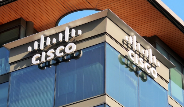 A low-angle exterior shot of a modern office building featuring prominent white Cisco logos mounted on two sides of its dark glass facade.