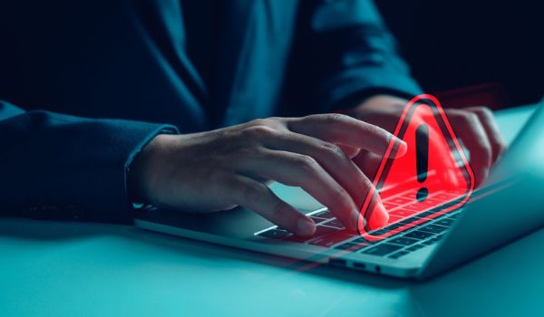 A person typing on a laptop with a glowing red warning icon over the keyboard.