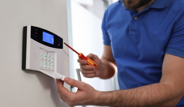 Man installing home security system on white wall in room