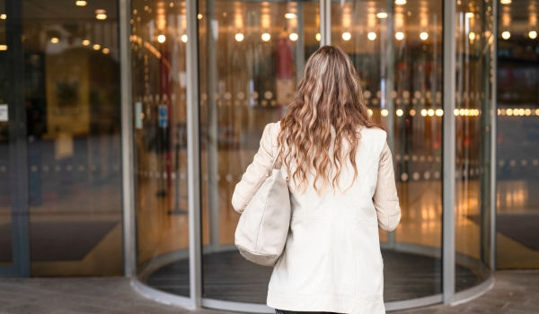 Woman walks toward a revolving door at a shopping center entrance during the late afternoon