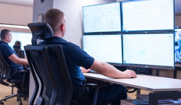 Operator seated at a workstation reviewing four monitors in a control room.