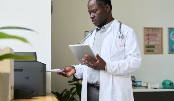 doctor holding medical documents while standing next to printer in well-lit medical office