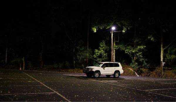 A lone white 4WD car under a street light in an empty parking lot at night